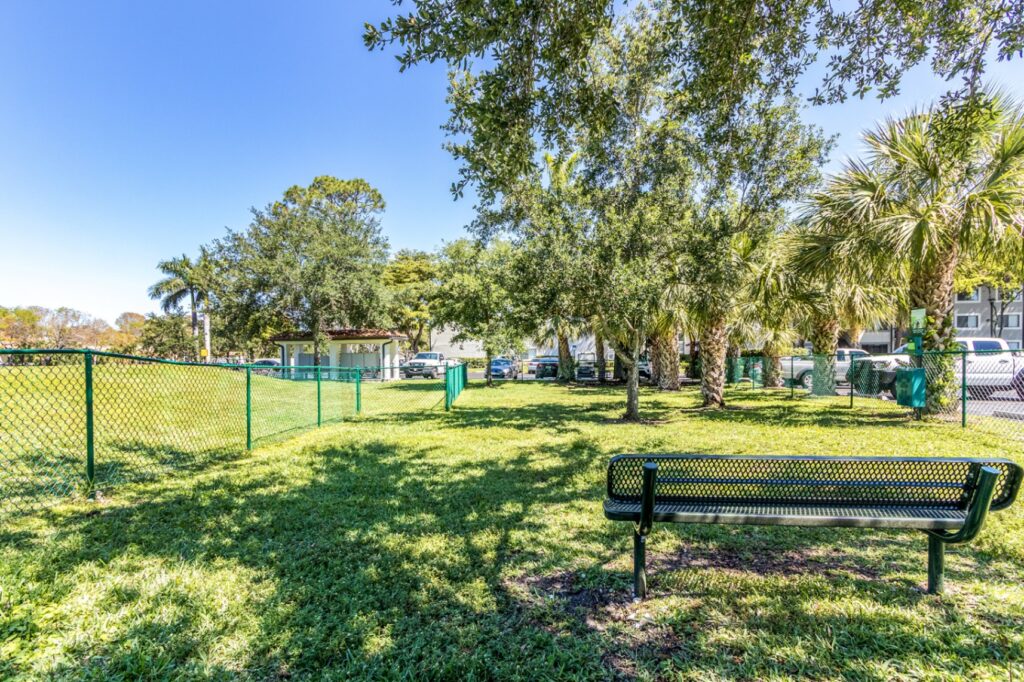 Fenced in dog park with bench, trash area, and trees.