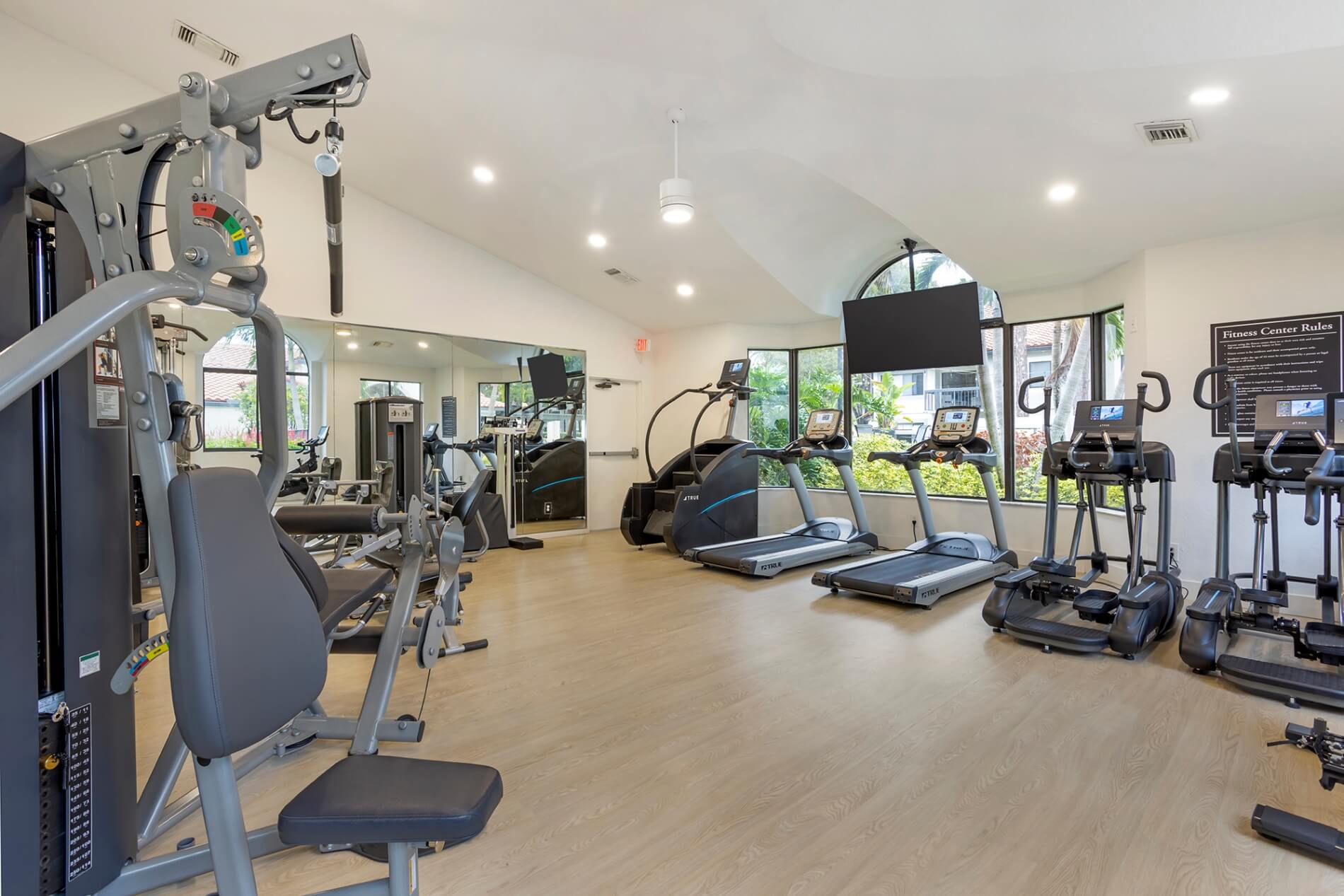 Fitness center with cardio and strength training equipment. Tv mounted on the wall.